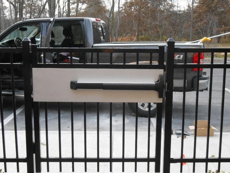 Black pickup truck behind a metal gate in a snowy driveway, with a cardboard box on the ground