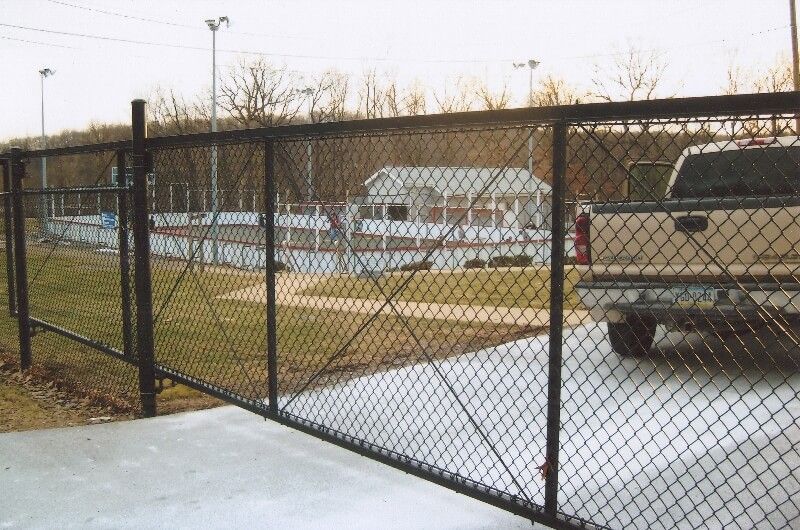 Chain-link gate beside a snowy parking lot with a white truck and building in the background