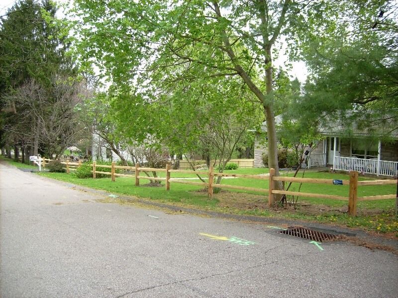 Tree-lined park path beside a wooden fence and grassy field on a cloudy day