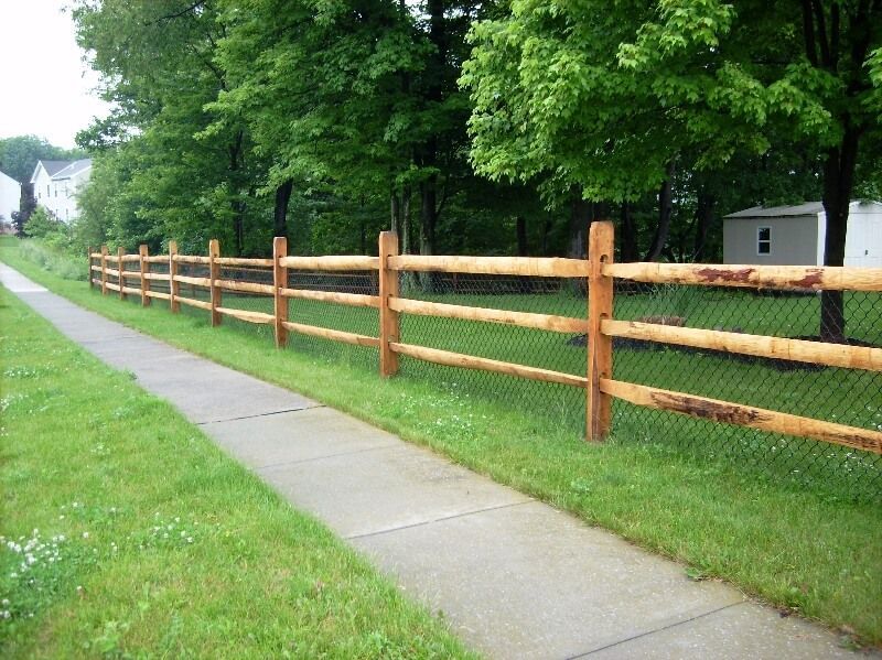 Wooden split-rail fence along a sidewalk beside a grassy yard and trees