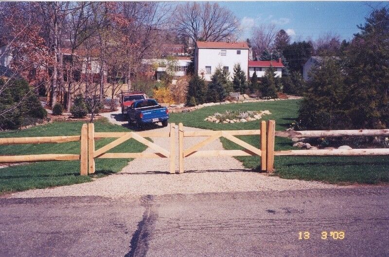 Wooden gate blocking a driveway in front of a house, with a blue car parked beyond it.