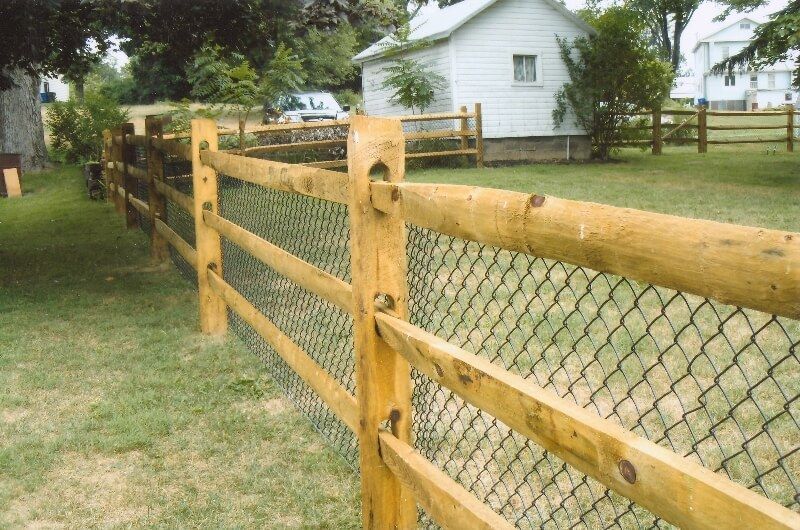 Wooden post-and-wire fence along a grassy yard with a white house in the background