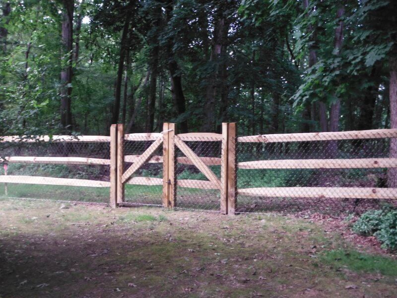 Wooden fence gate opening onto a wooded path in a forest clearing.