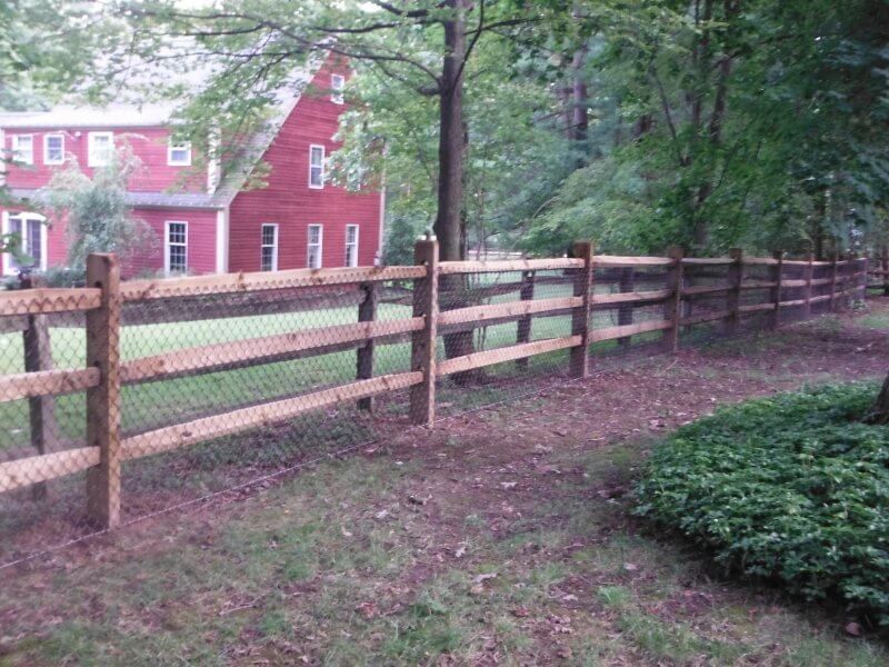 Wooden split-rail fence beside a yard and red house surrounded by trees