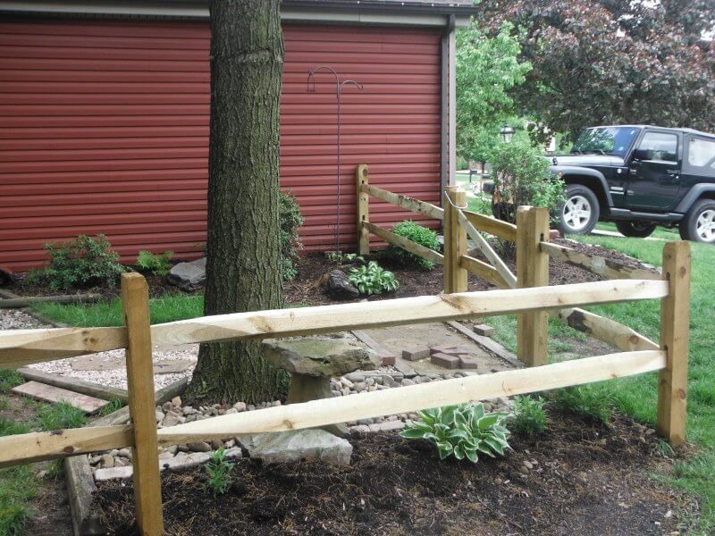 Wooden fence enclosing a garden bed beside a red garage, with a Jeep in the background.