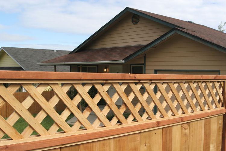 Wooden lattice fence in front of a house with a brown roof and beige siding