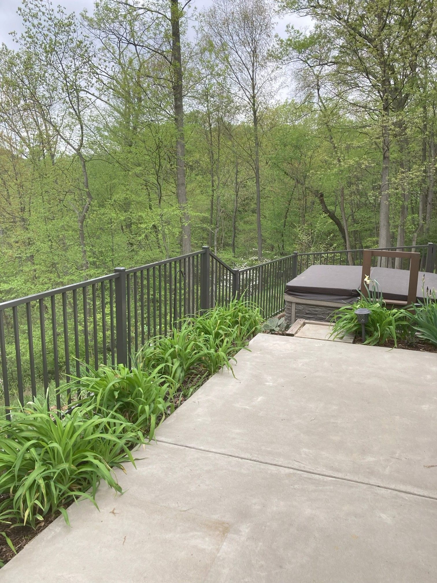 Concrete patio overlooking a green wooded area, with a black railing and outdoor seating.