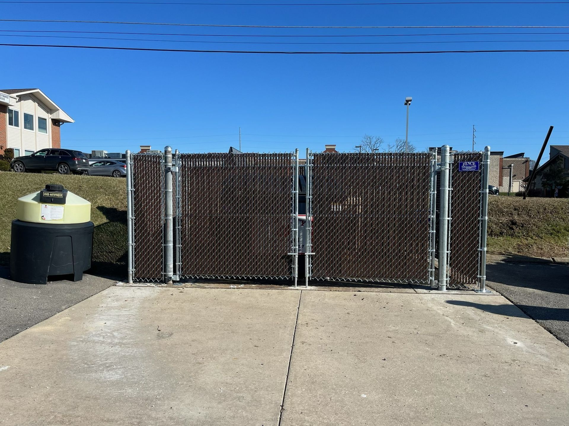 Closed metal gate blocking a concrete driveway beside a trash can under a clear blue sky