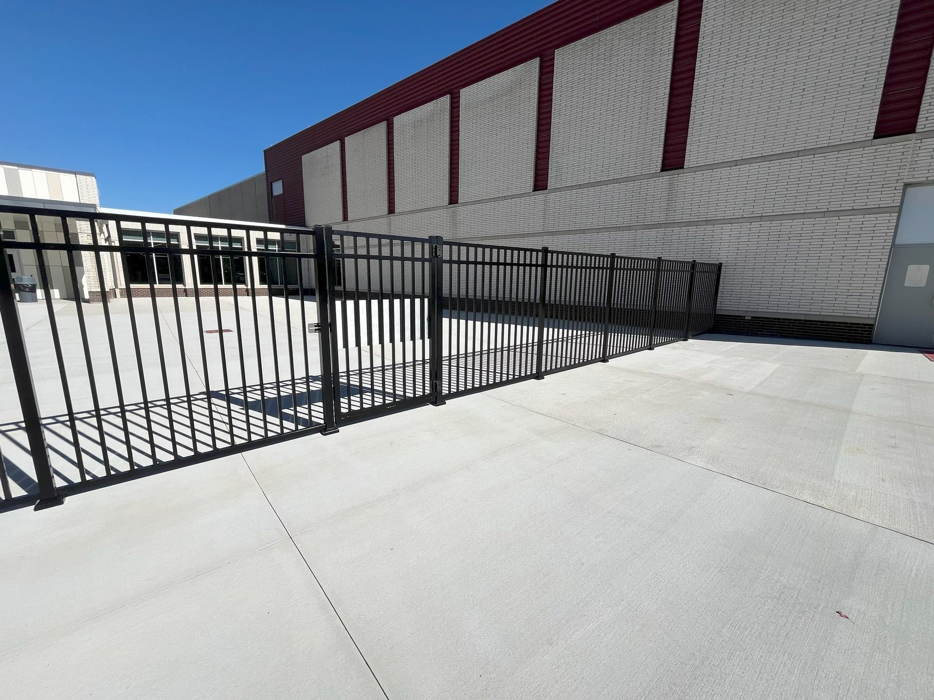 Empty concrete courtyard with black metal fence beside a white building with red trim.