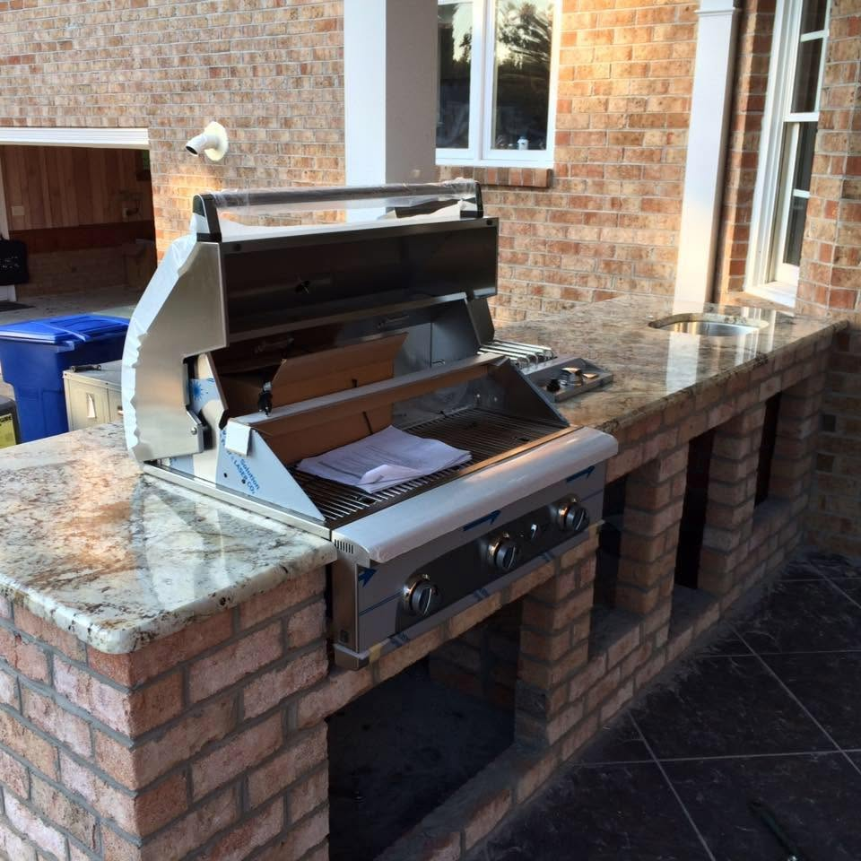 Built-in outdoor grill on a brick patio beside a house, with granite countertop and sink.