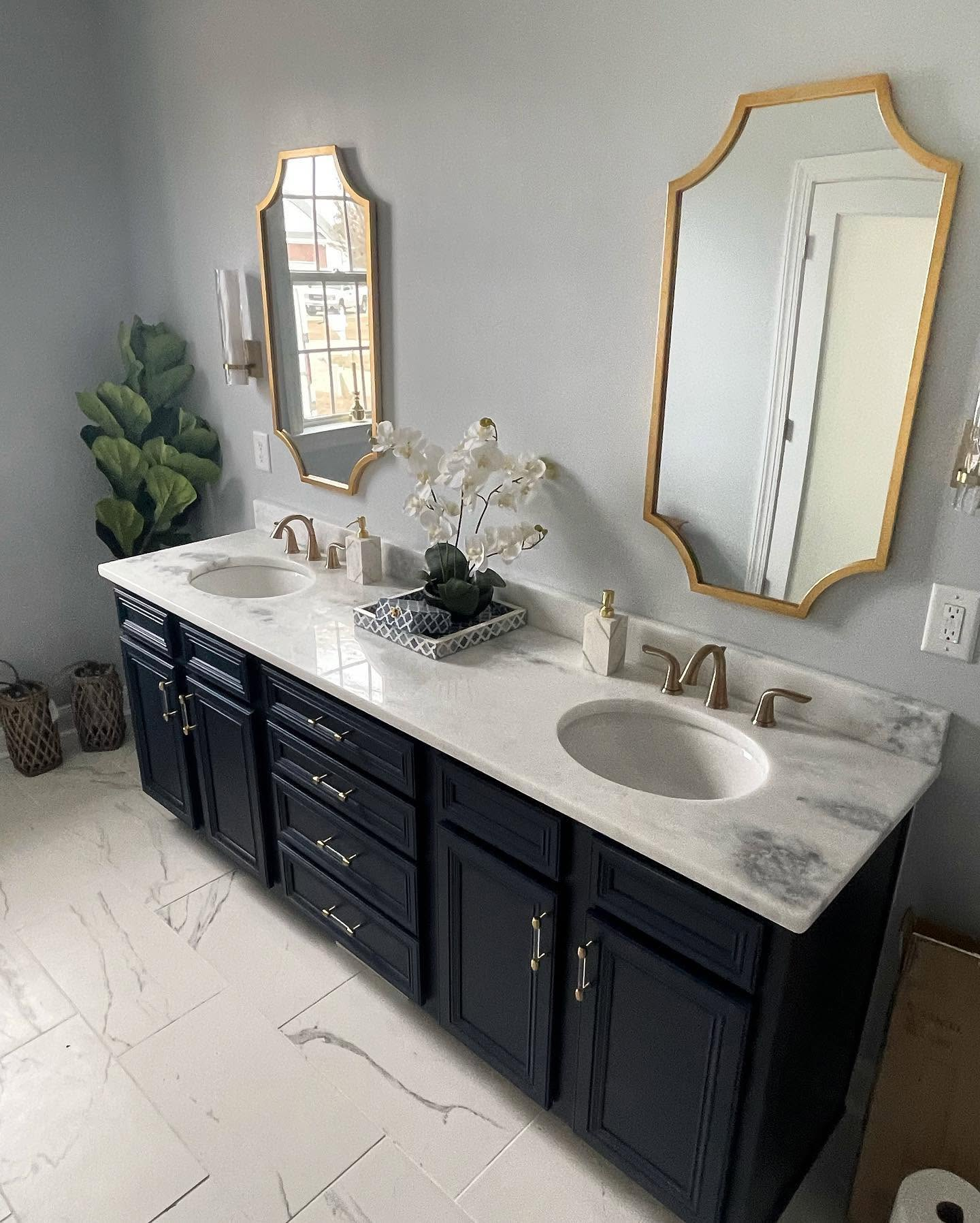 Modern bathroom vanity with dark cabinets, white countertop, two gold-framed mirrors, and double sinks