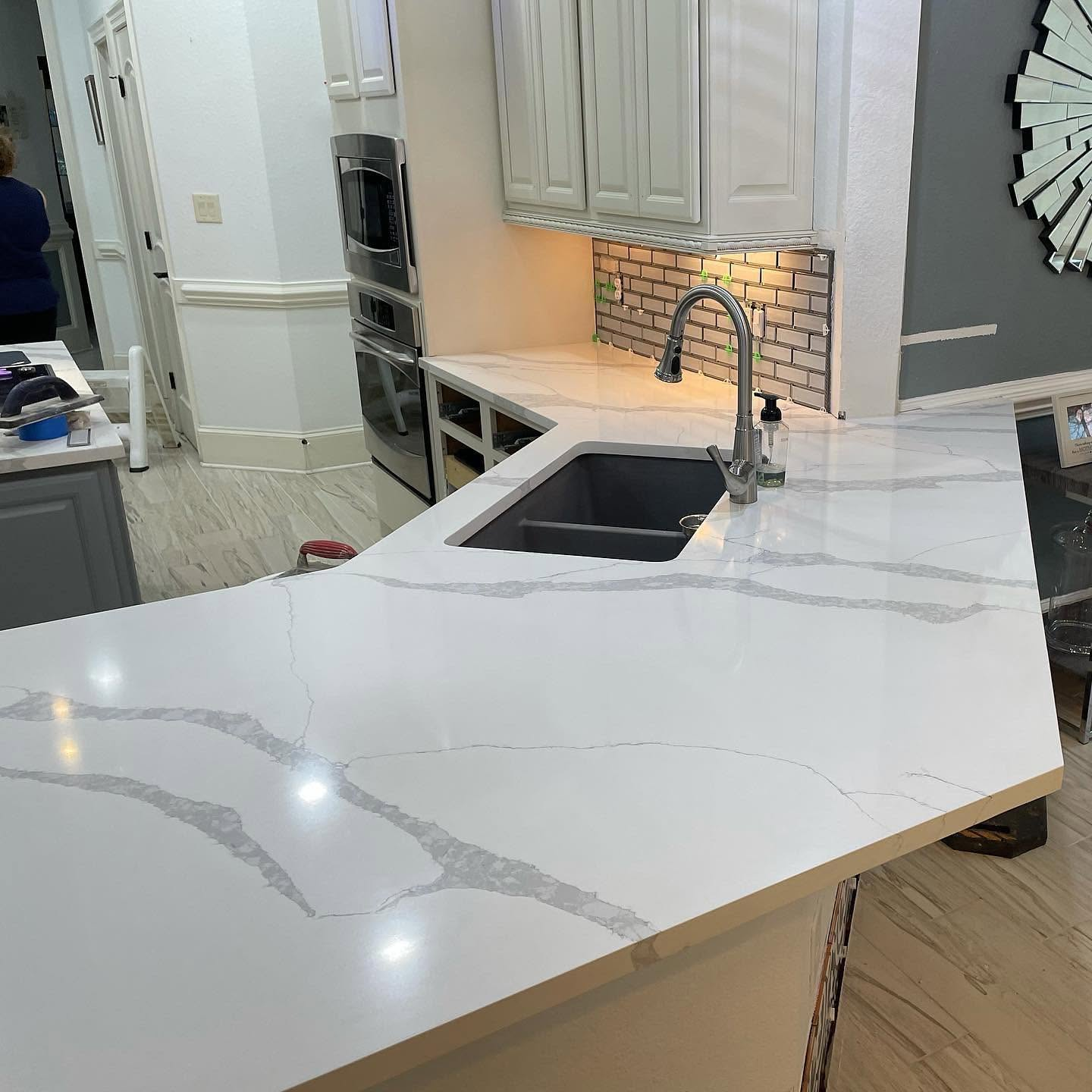 Modern kitchen island with white marble countertop, black sink, chrome faucet, and built-in oven cabinets