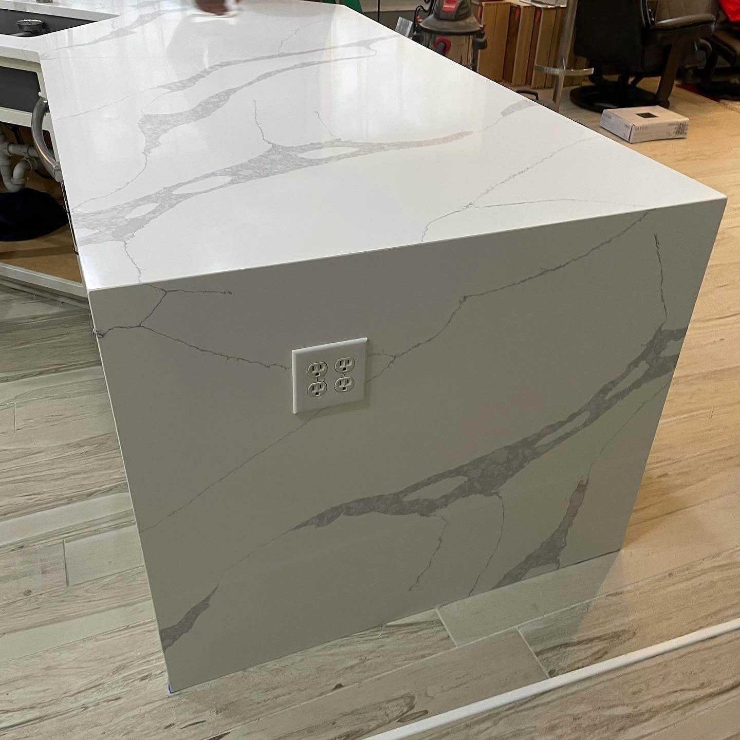 White marble-look kitchen island with a built-in outlet on the side in a showroom setting
