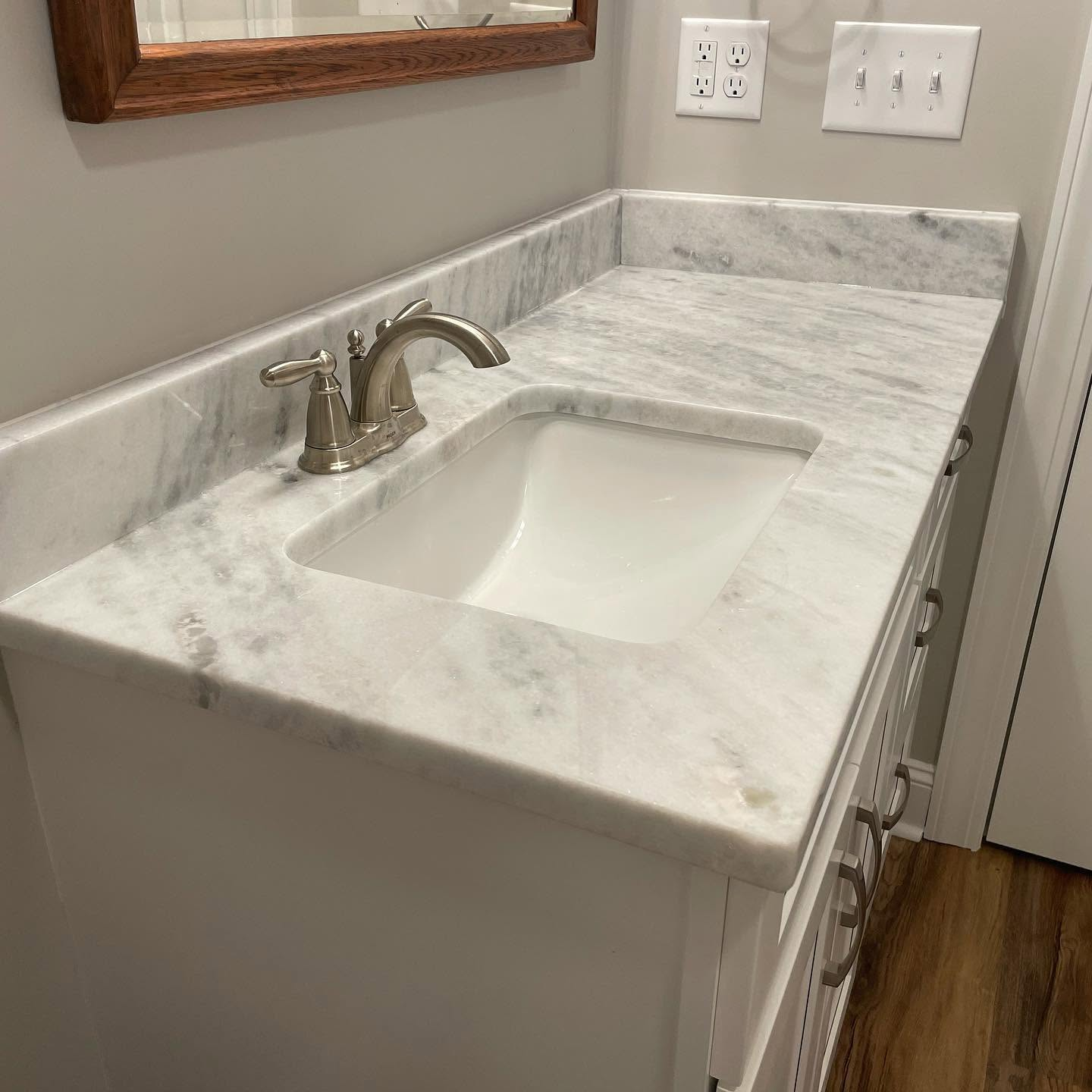 Marble bathroom vanity with rectangular sink, brushed-nickel faucet, mirror, and wood floor.