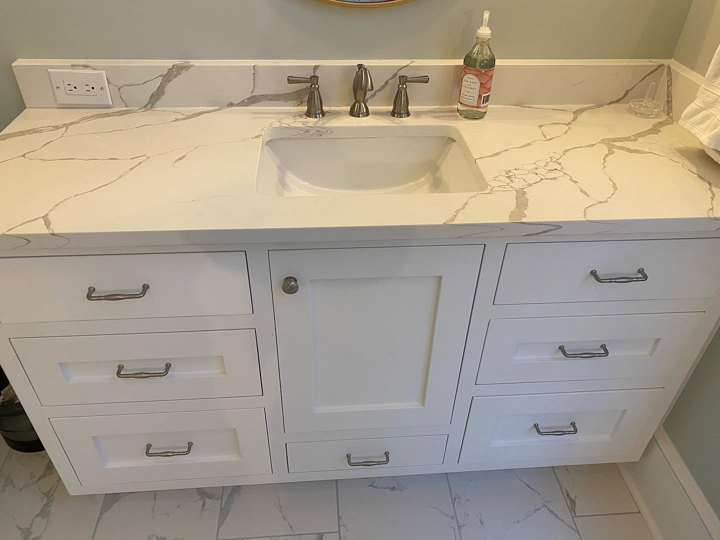 White bathroom vanity with marble countertop, sink, faucet, and built-in cabinet drawers.