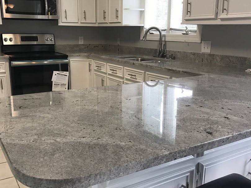 Modern kitchen with granite island, white cabinets, stainless steel stove, and window over sink
