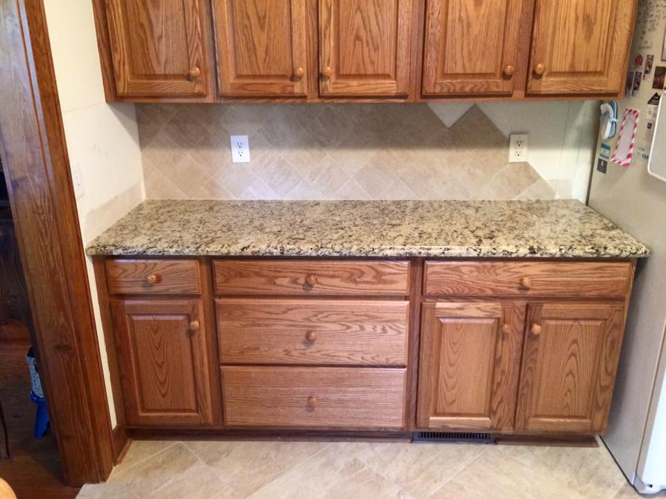 Wooden kitchen cabinets with granite countertop against a beige tiled wall