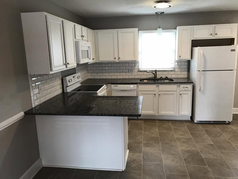 Empty kitchen with white cabinets, black countertops, gray tile floor, and white refrigerator.