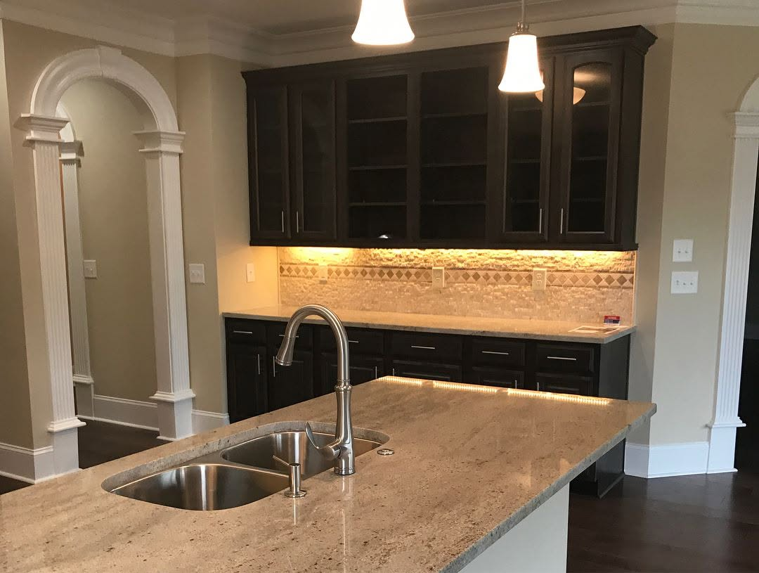 Modern kitchen with granite island, double sink, dark cabinets, and arched entryways