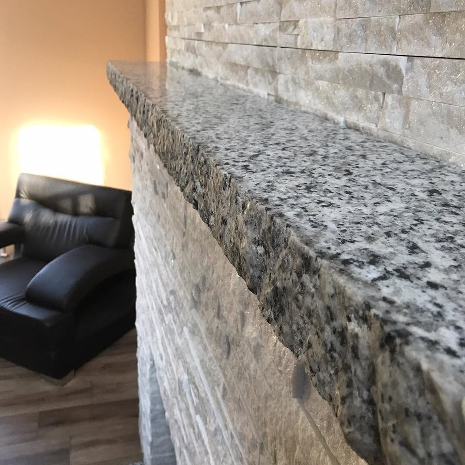 Close-up of a granite ledge beside a stone wall, overlooking a living room with a black chair and lamp.