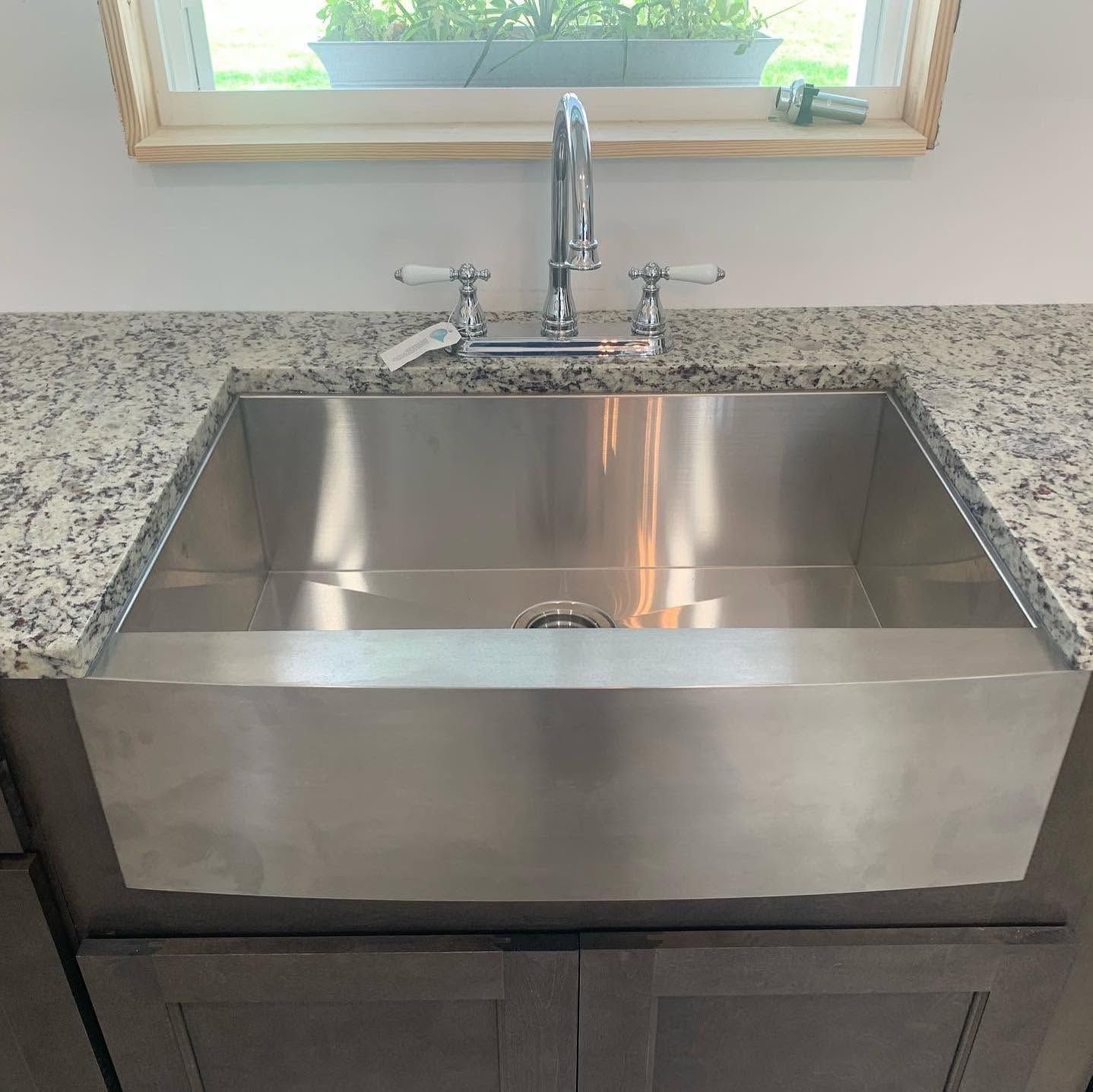 Stainless steel farmhouse sink with chrome faucet set in a speckled granite countertop beneath a window.