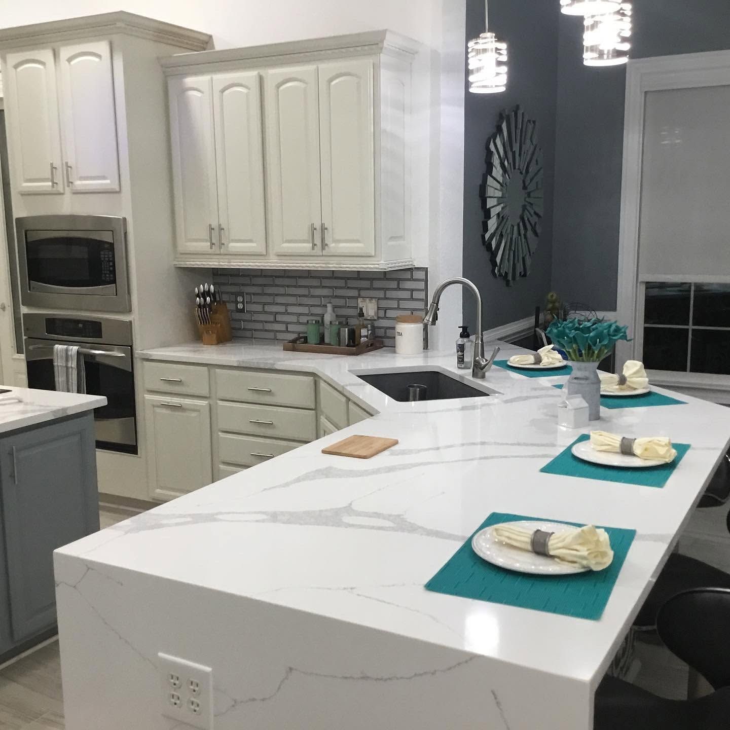 Modern white kitchen with marble island, teal placemats, and built-in stainless appliances
