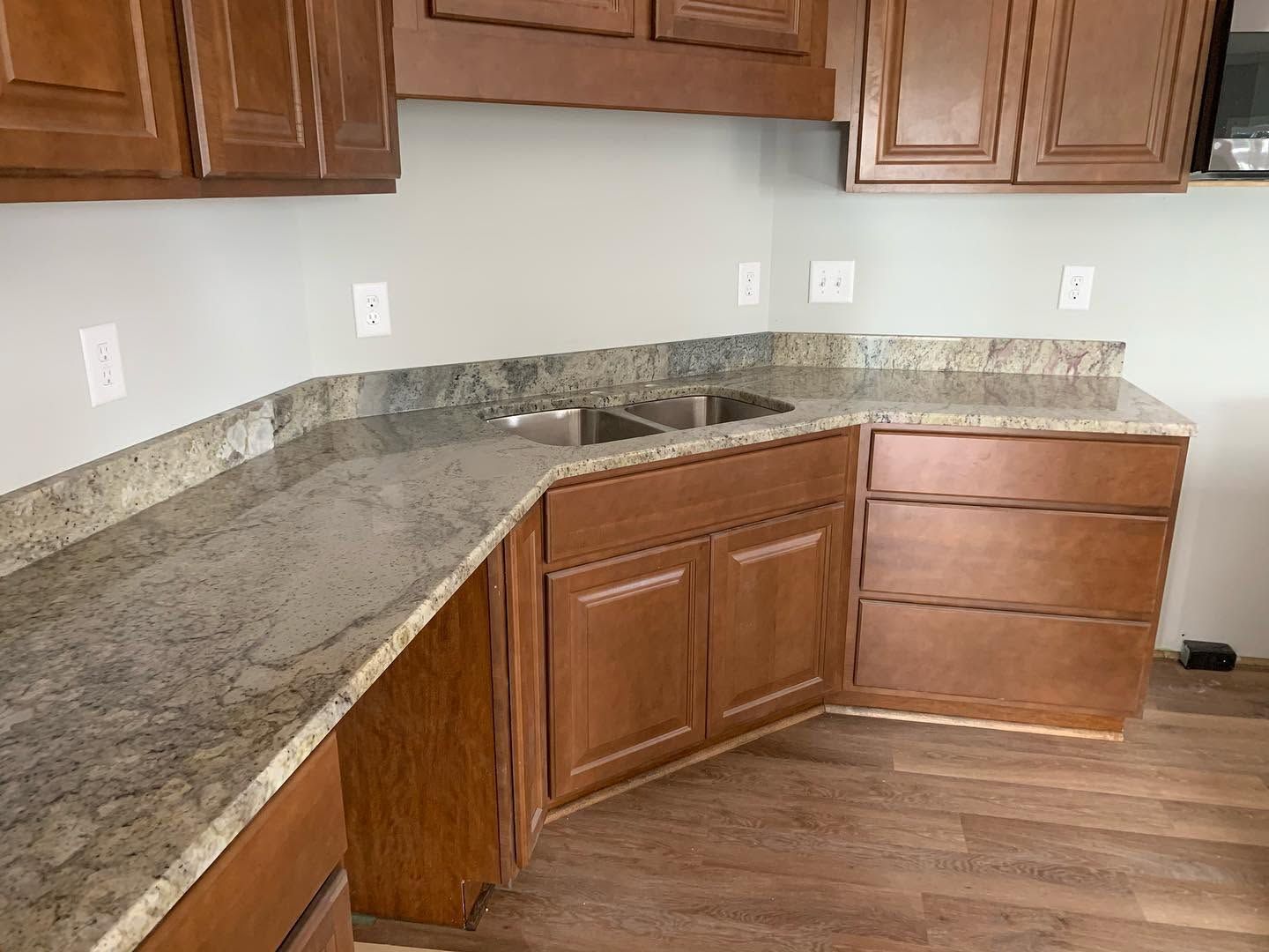 Empty kitchen with wood cabinets, gray granite countertops, and wood flooring