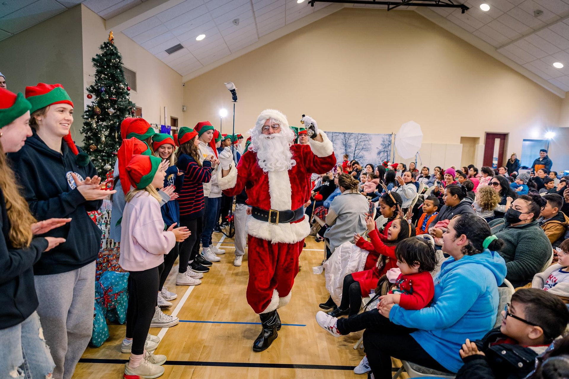 Santa claus is walking through a crowd of people in a gym.