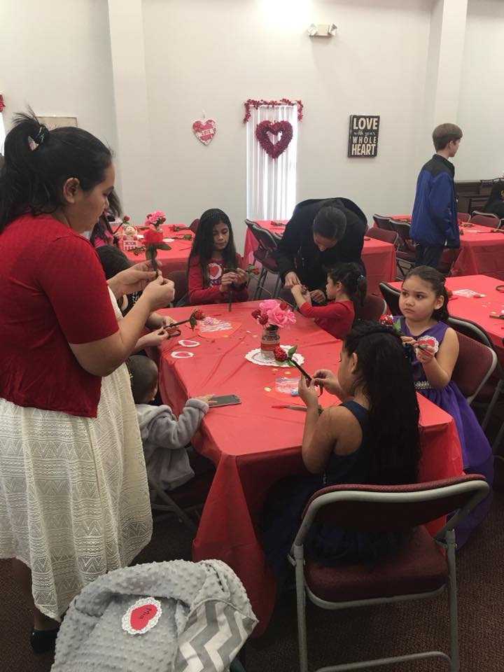 A woman in a red shirt is standing in front of a group of children sitting at tables