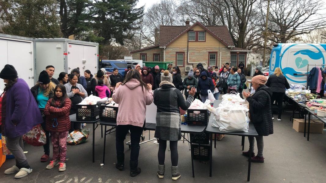 A large group of people are standing around tables in a parking lot.