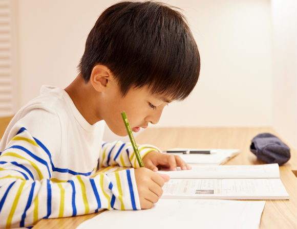 A boy writing at a desk, focused on a book and paper.