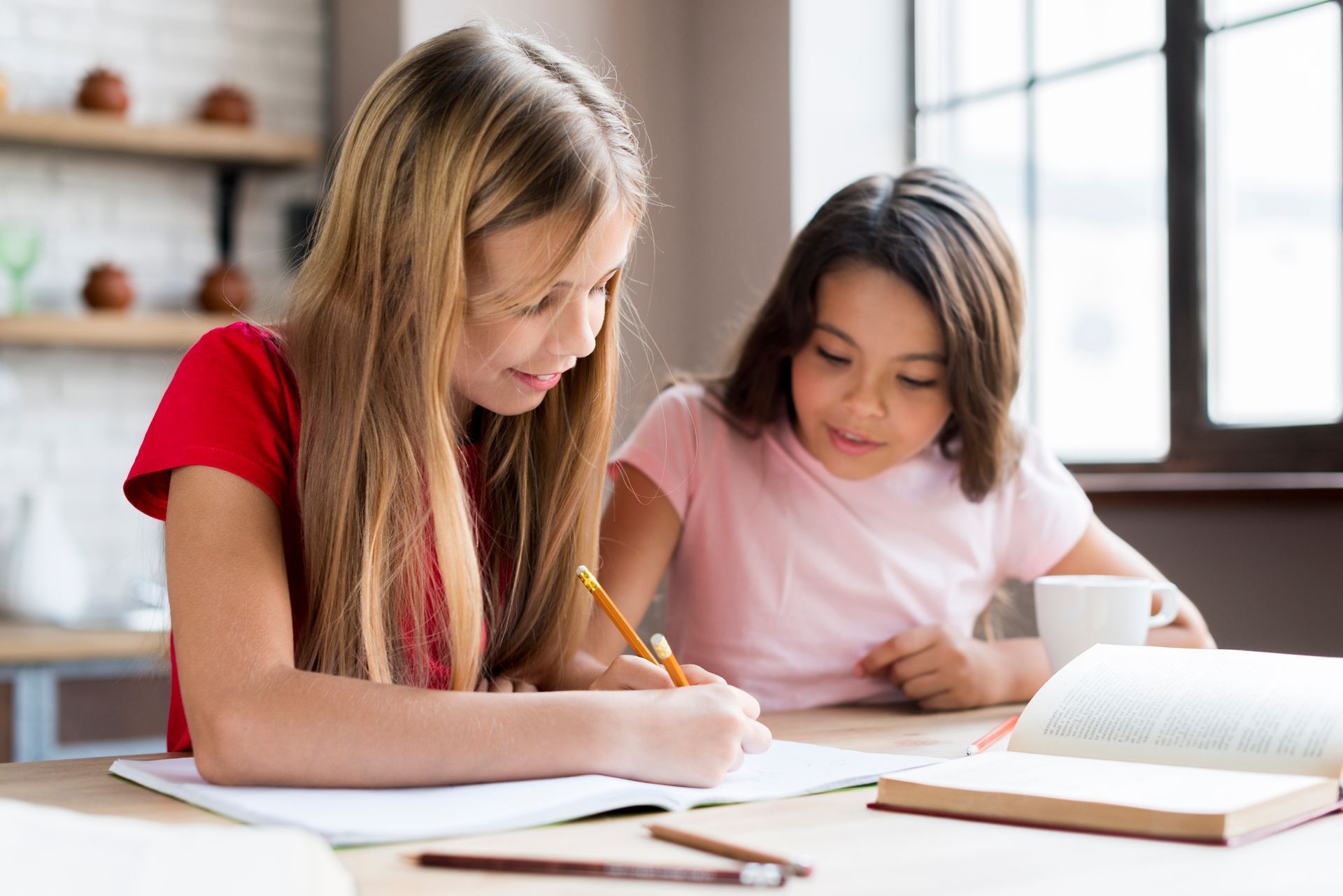 Two young girls are sitting at a table doing their homework.