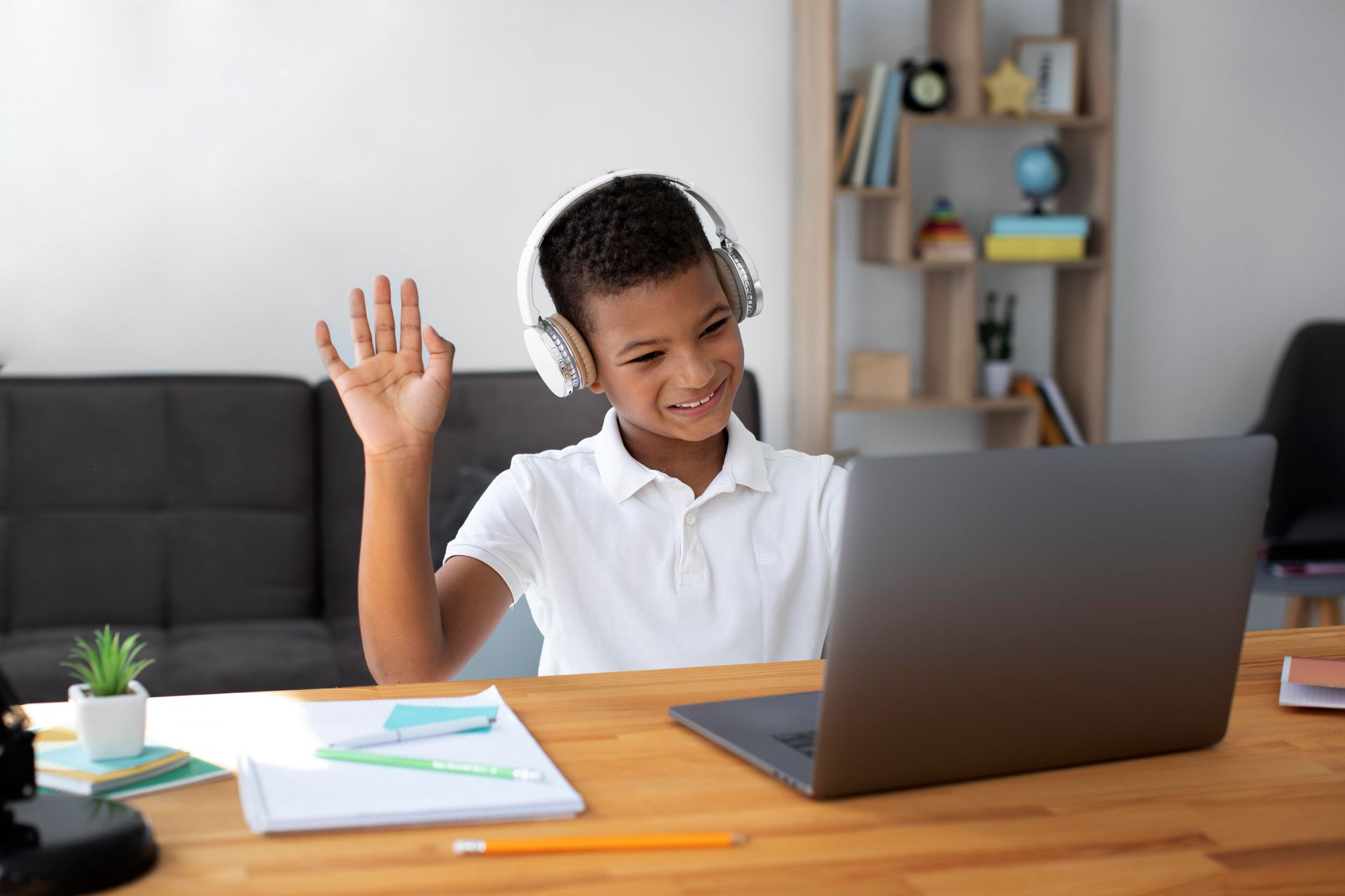 A young boy wearing headphones is sitting at a desk using a laptop computer.