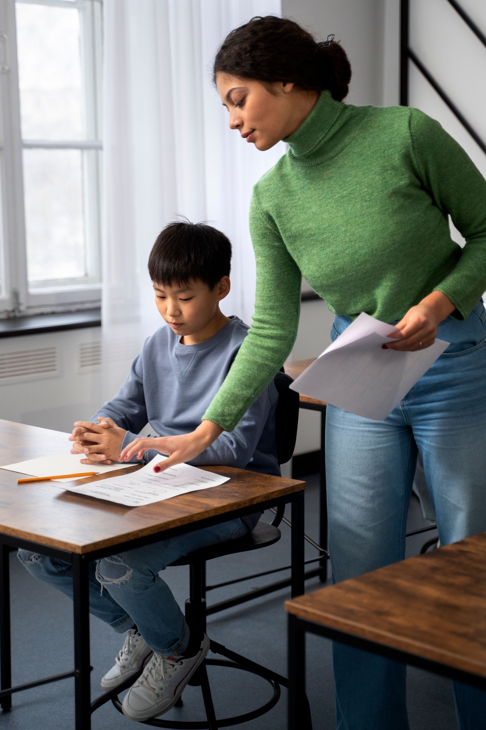 A woman tutor is helping a young boy with his homework in a classroom.