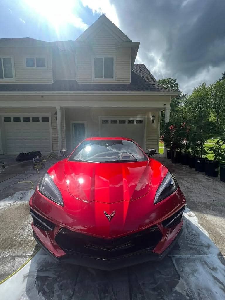 Red sports car parked in a sunny driveway in front of a two-story house