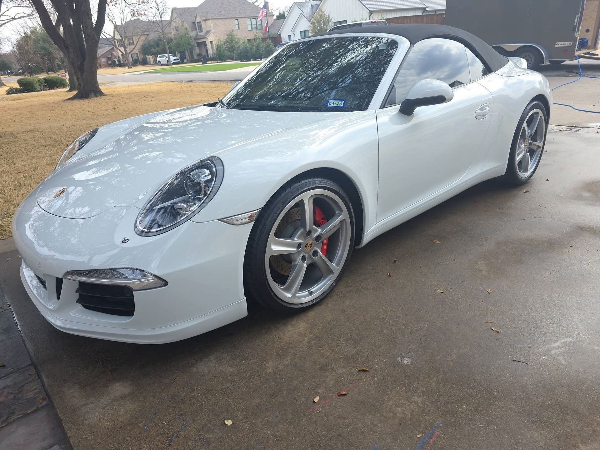 White convertible sports car parked on a wet driveway in a residential neighborhood