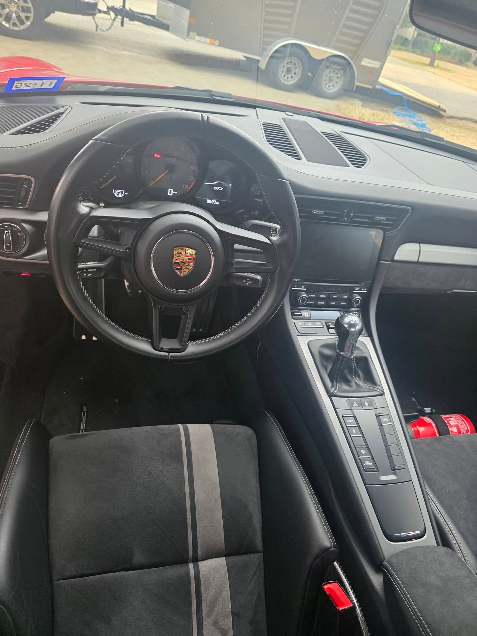 Porsche interior with steering wheel, center console, and black seats; dashboard view from the driver’s side