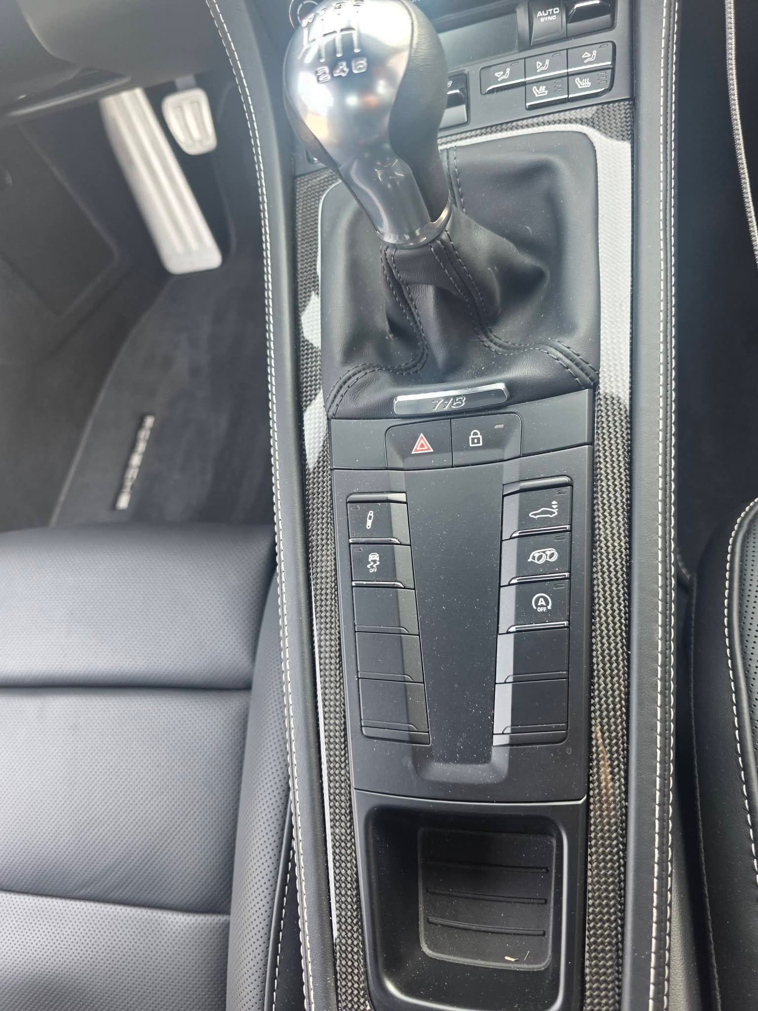 Car center console with gear shift and climate control buttons beside a black leather seat.