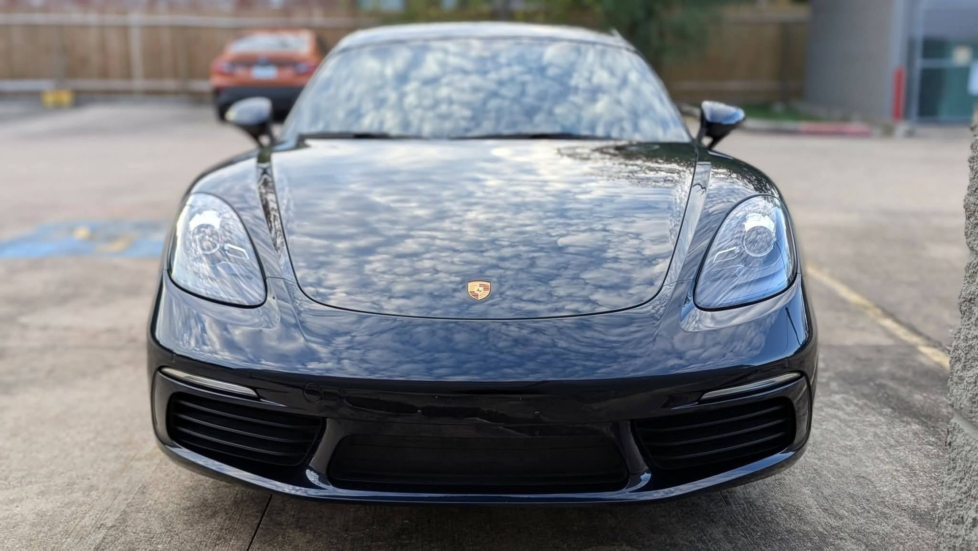Front view of a black Porsche sports car parked on a concrete lot