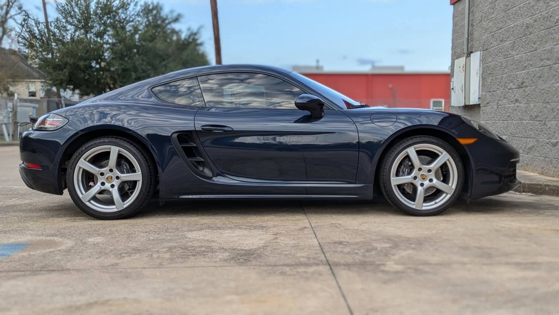 Black sports car parked side view on a concrete driveway beside a building