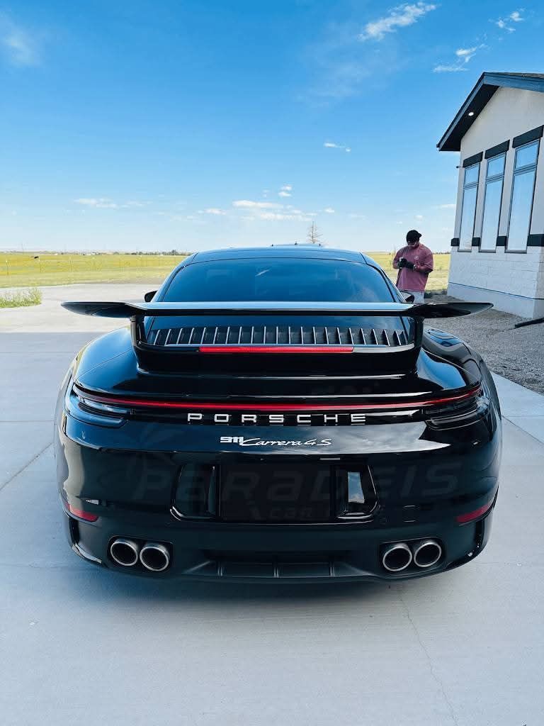 Black Porsche 911 parked on a runway, rear view with large spoiler and a person standing nearby