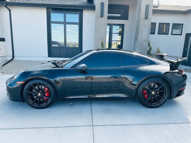Black sports car parked in a modern driveway beside a white house