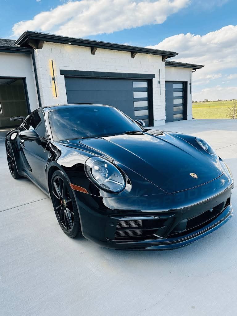 Black sports car parked in front of a white garage under a bright sky