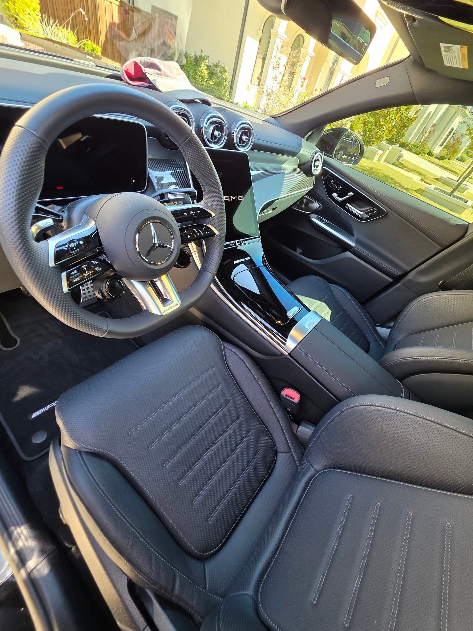 Luxury car interior with black leather seats, Mercedes steering wheel, and sunlight through the windows