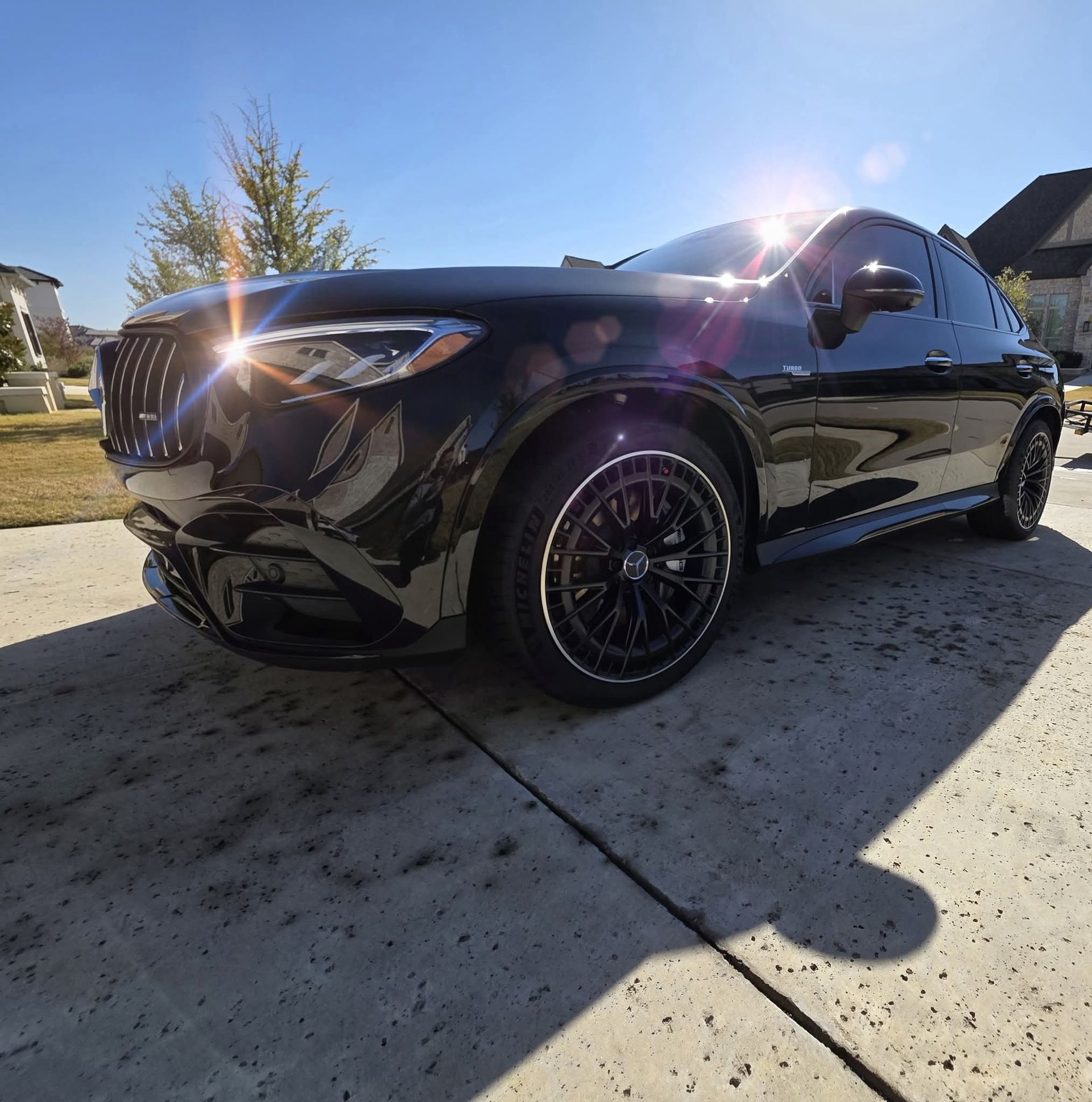 Black SUV parked in a sunny driveway, low-angle view with bright sun glare.