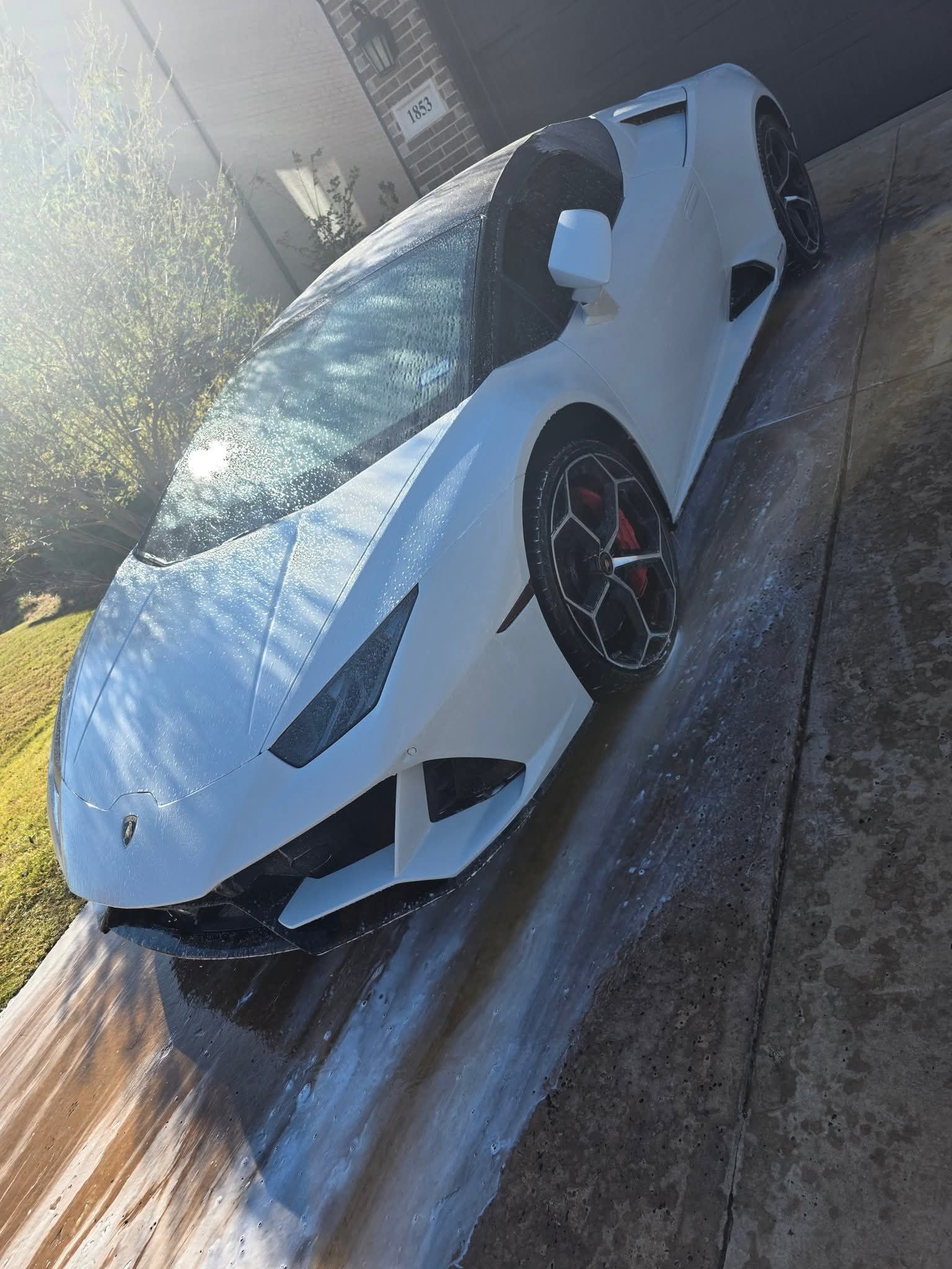 White sports car parked on a driveway in sunlight, viewed at an angle from the front.
