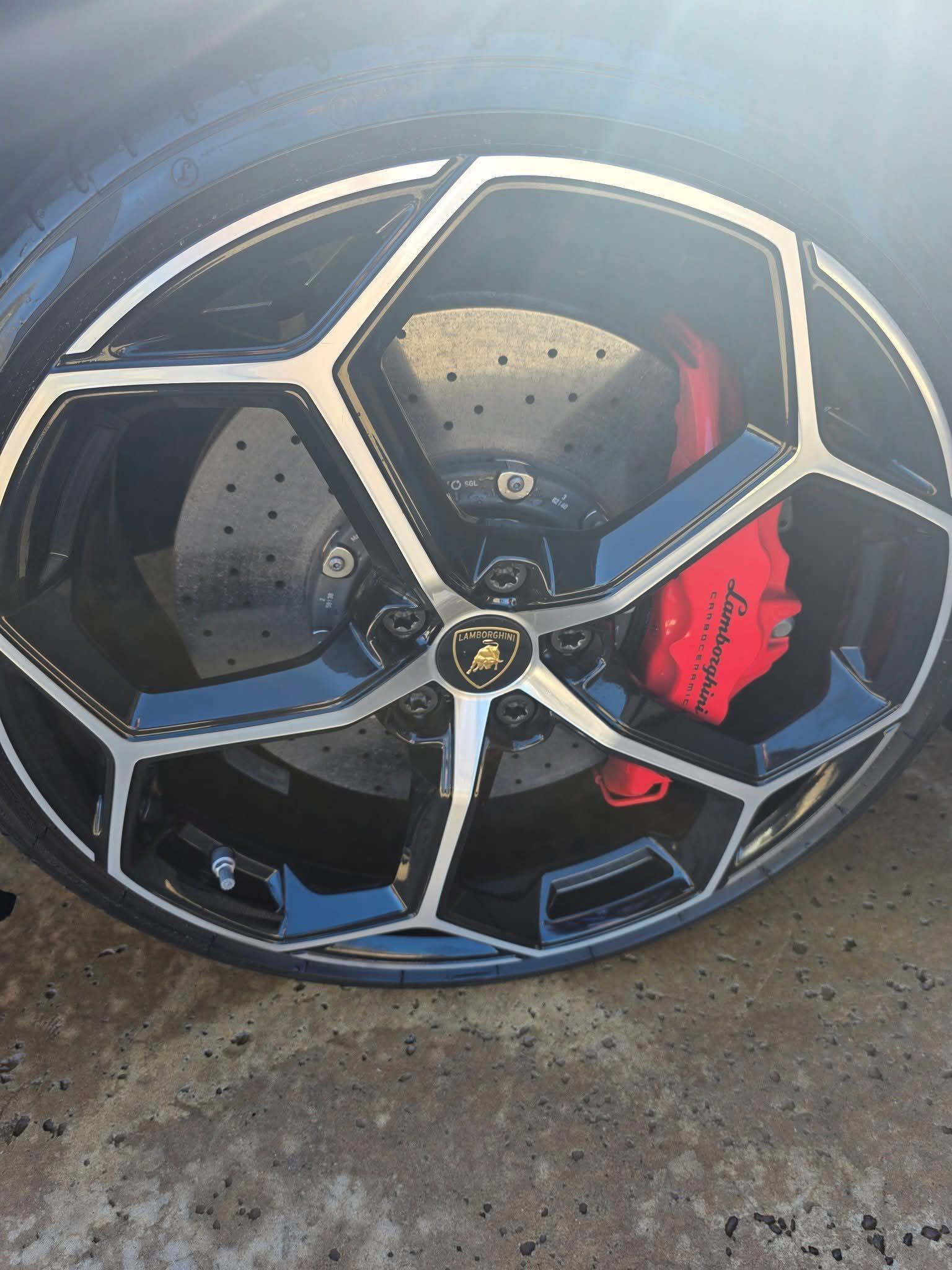 Damaged black and silver car wheel rim with red brake caliper on pavement