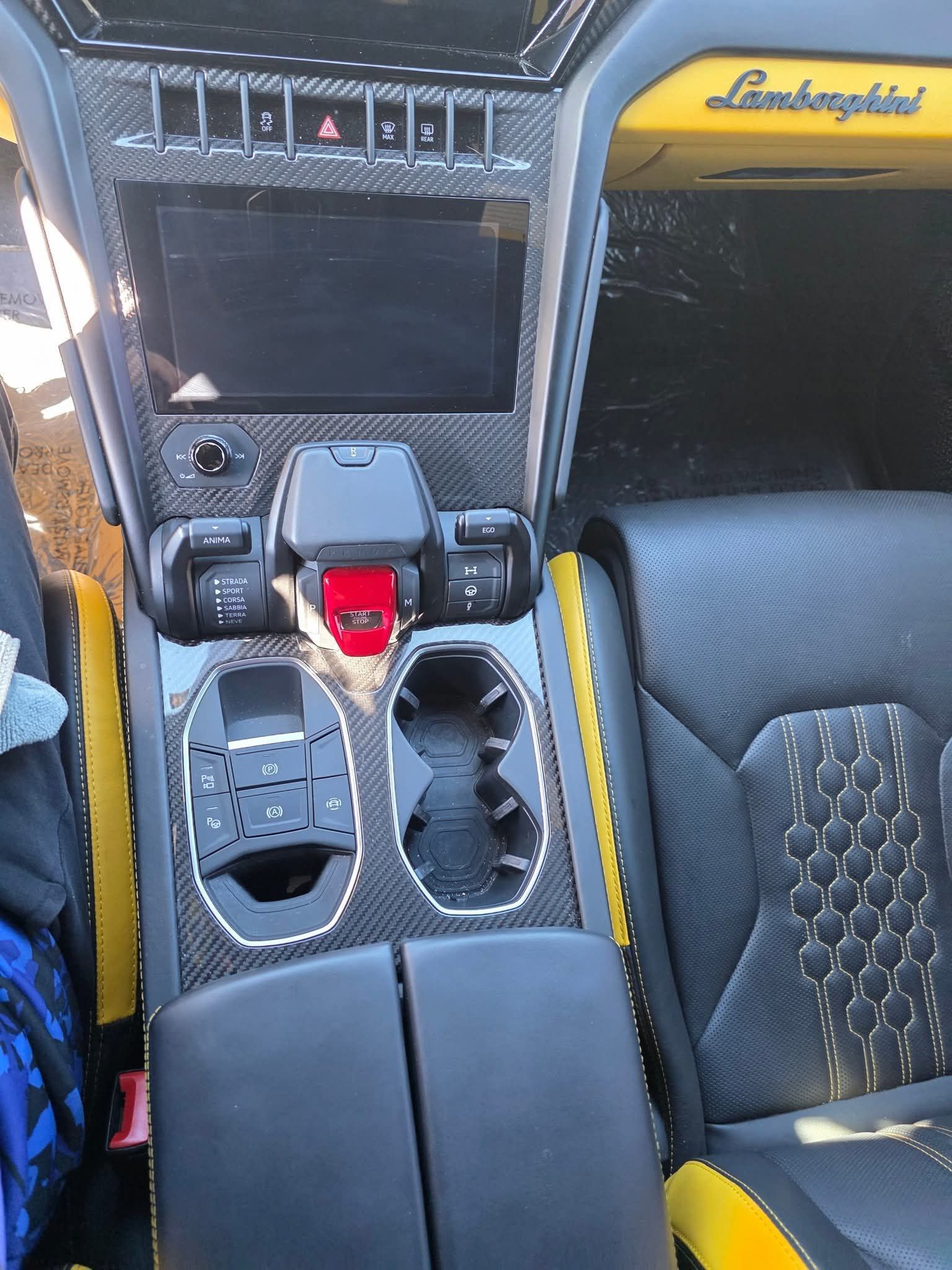 Car interior with Lamborghini-style dashboard, center console, cup holders, and black-and-yellow seats