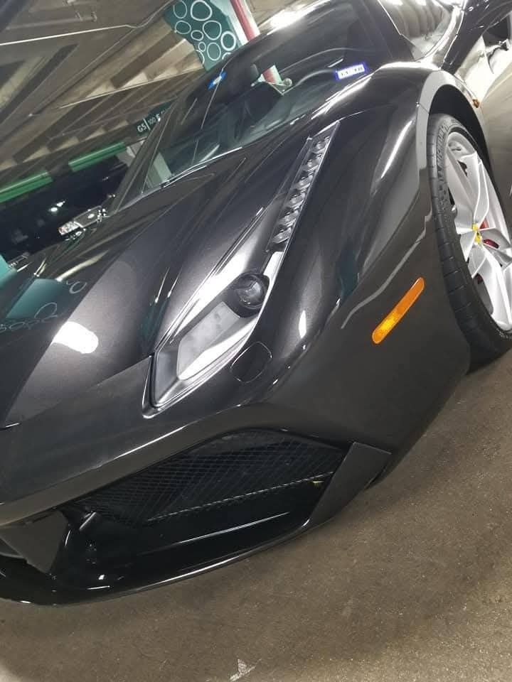 Black sports car angled indoors, showing sleek front end and silver wheels.