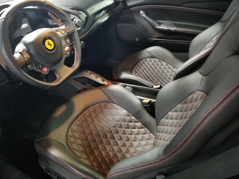Ferrari interior with black leather seats, red stitching, and steering wheel visible in the cockpit